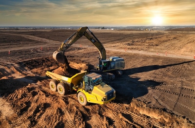 Efficient backhoe operation at sunrise, loading truck with sand exemplifying safety management by a professional safety consulting company.
